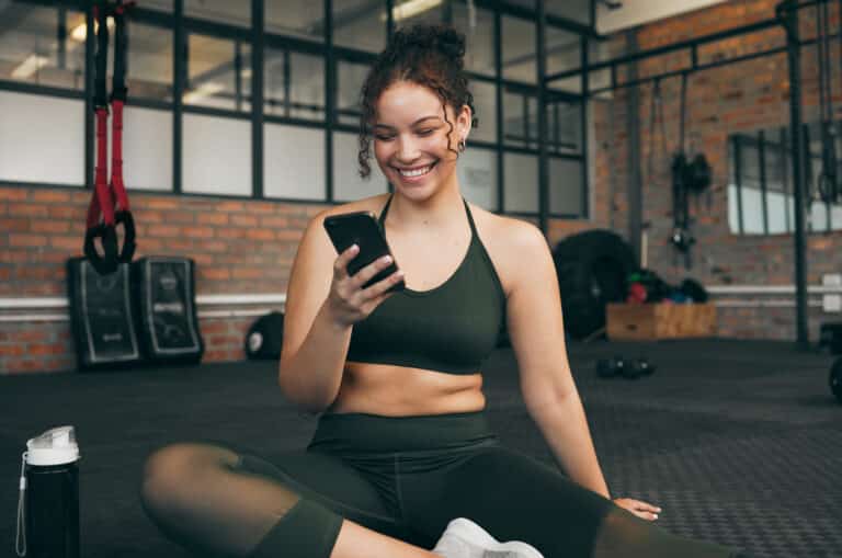 Happy woman, fitness and phone at gym for a workout, training and body wellness with a mobile app. Sports female with smartphone for progress, performance and communication for a healthy lifestyle.