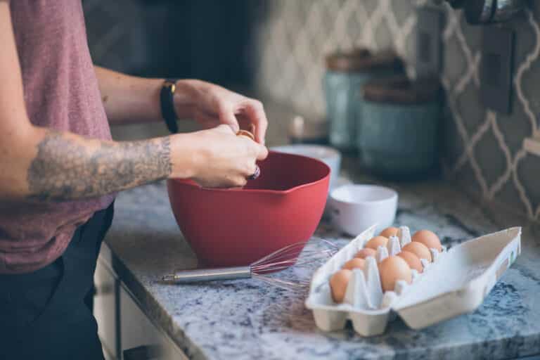 cropped image of woman cracking an egg into a red bowl in a grey kitchen