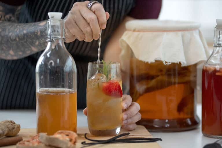 Tattooed woman preparing her kombucha tea in the kitchen, dietetic organic superfood healthy fermented tea