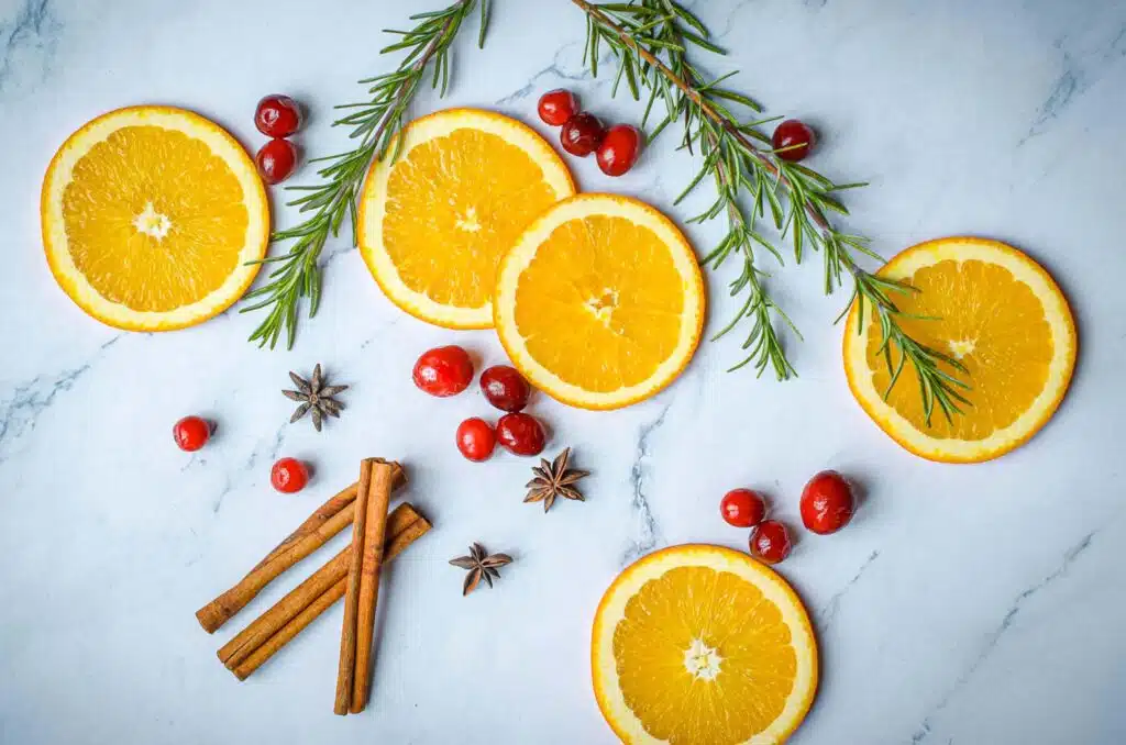 overhead shot of oranges, rosemary, cinnamon sticks, and cranberries to decorate a punch bowl