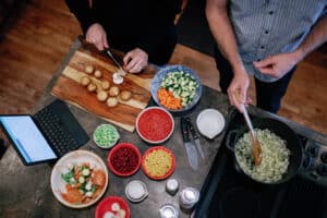 overhead shot of two people chopping food and stirring a pot to make soup