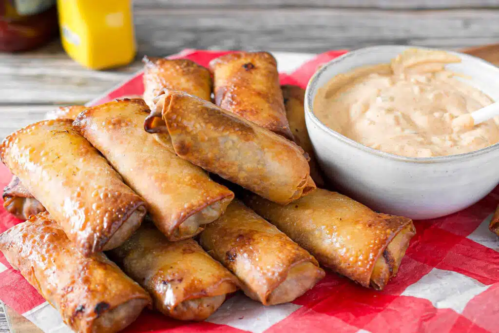 close up view of a stack of cheeseburger eggrolls next to a bowl a dipping sauce