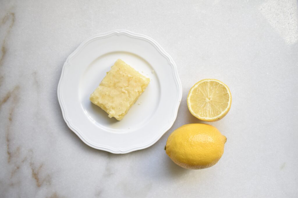 overhead shot of single lemon square on white plate with cut lemon next to it