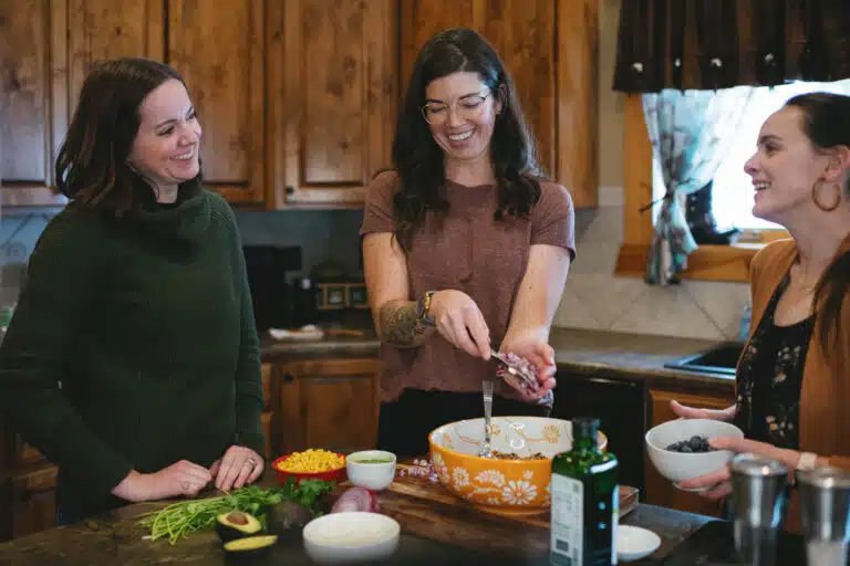 three women laughing and cooking together in a kitchen