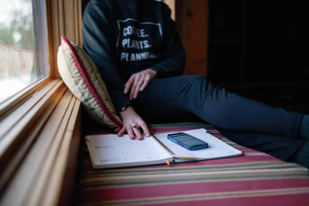 cropped image of woman sitting on a window bench with her planner and phone sitting in front of her