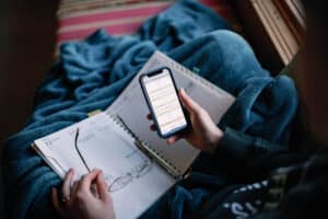 over the shoulder view of woman meal planning with a planner and her phone. Glasses in hand