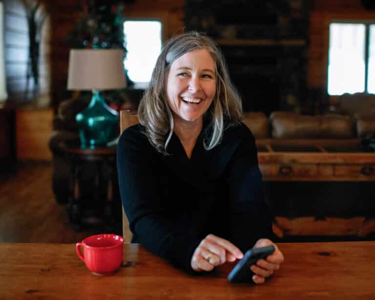 image of woman sitting at a table holding a phone, looking up laughing