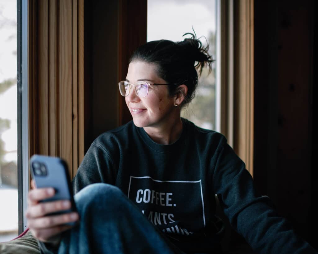 woman holding her phone, gazing out the window